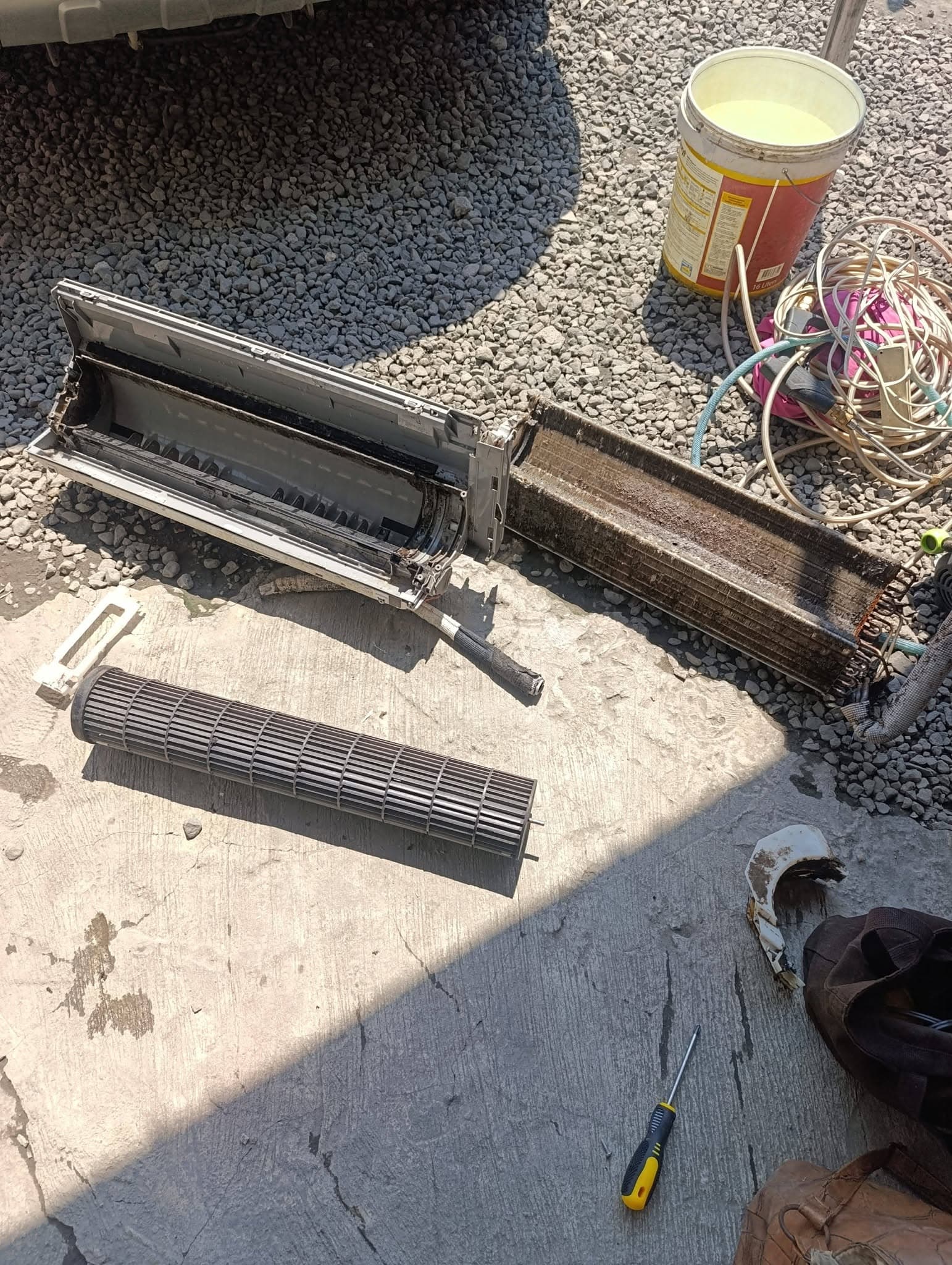 Disassembled split-type indoor air conditioner with dirty housing, coil, and blower wheel laid out for cleaning.