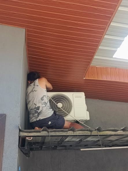 Technician servicing an outdoor inverter condenser from an elevated platform.