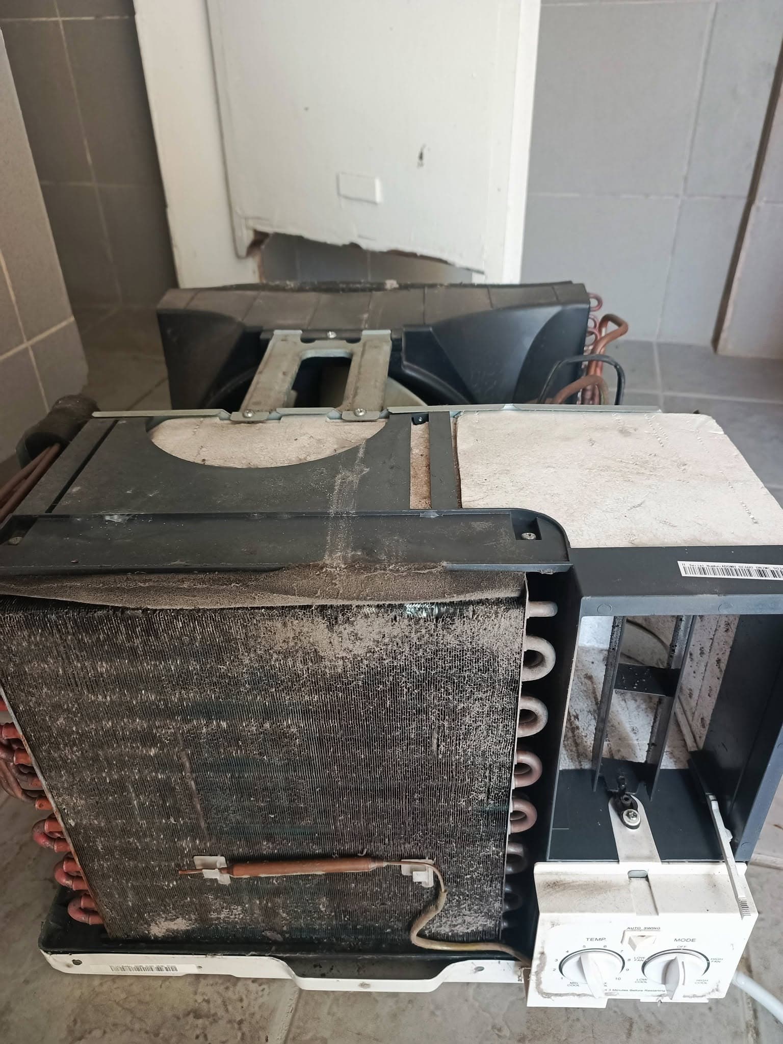 Dust-clogged window-type air conditioner opened for inspection before deep cleaning.