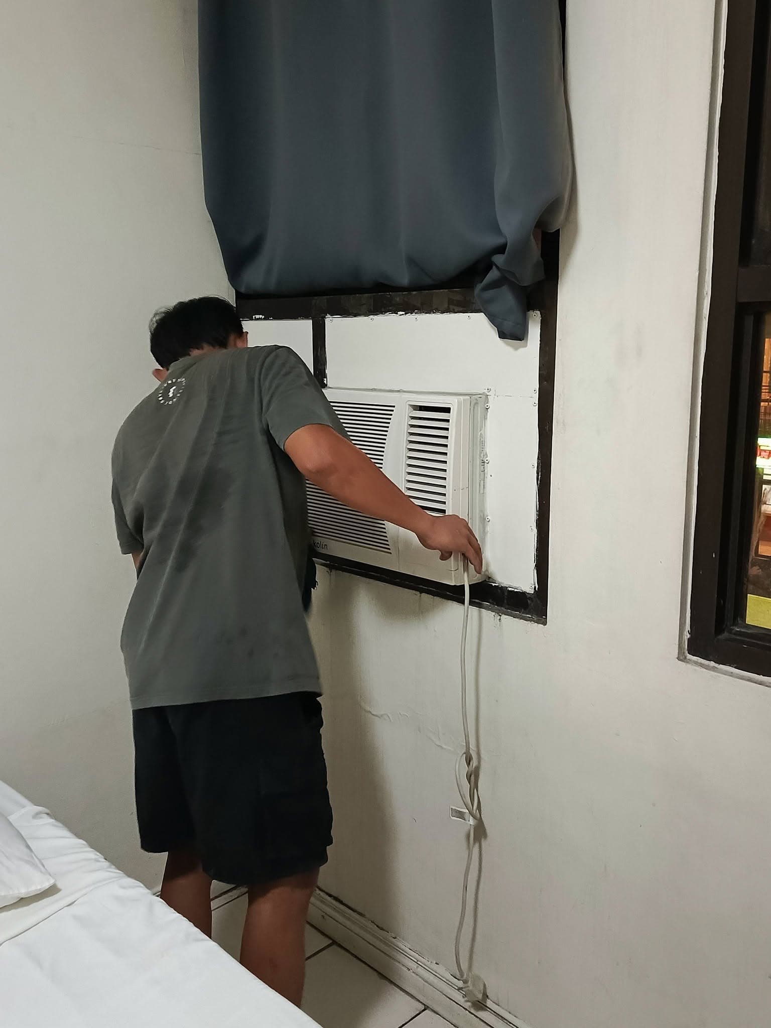 Technician reinstalling the cleaned window-type air conditioner in a guest room.