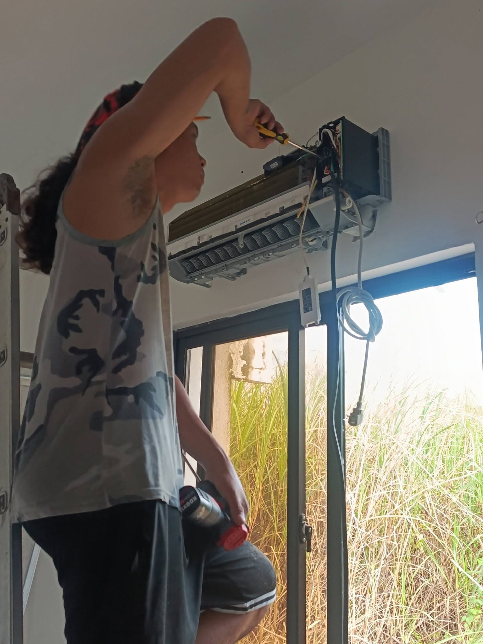 Technician connecting wiring inside the open indoor air-conditioning unit.