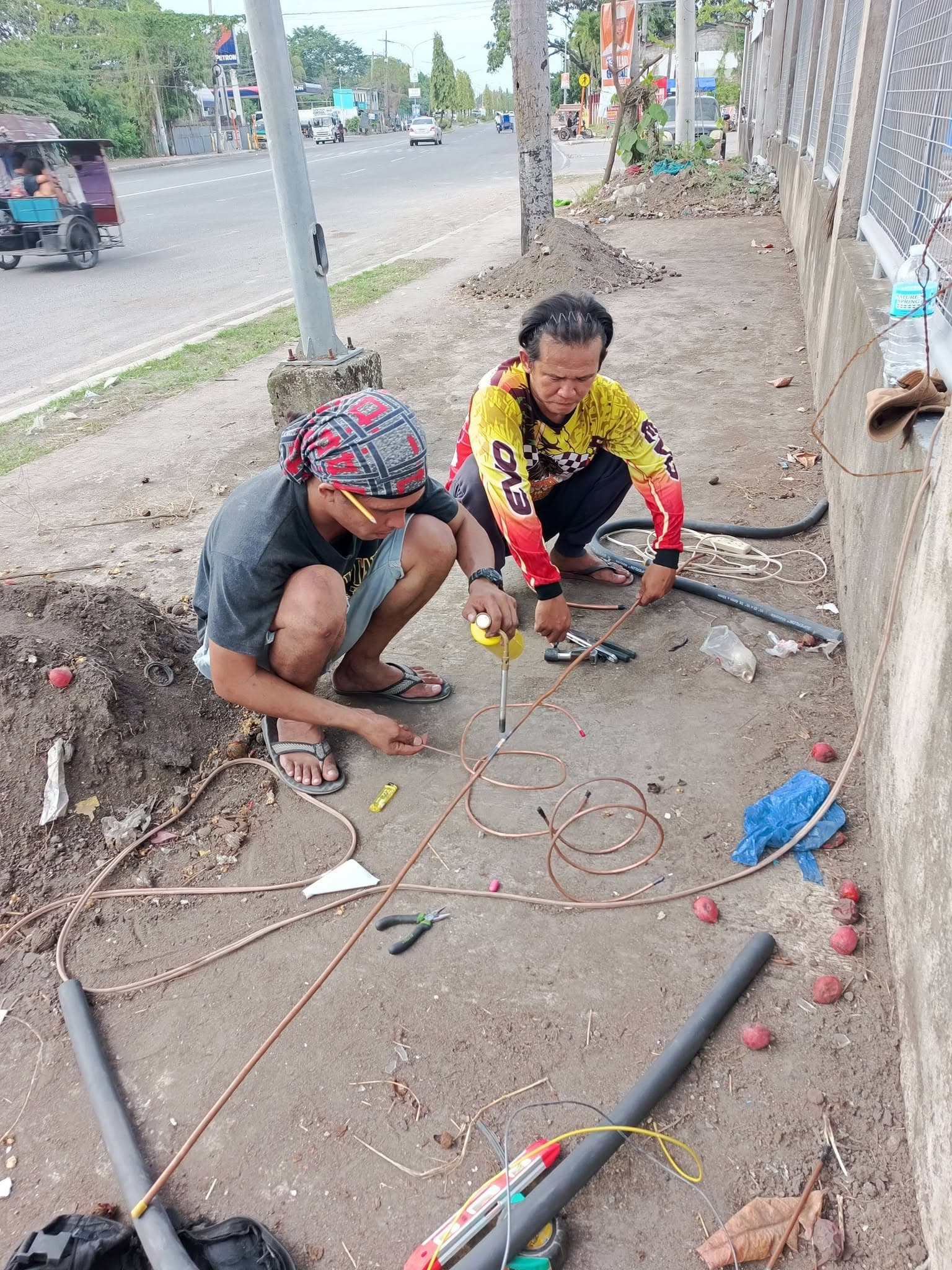 Two technicians preparing and brazing copper refrigerant lines for a split-system installation.