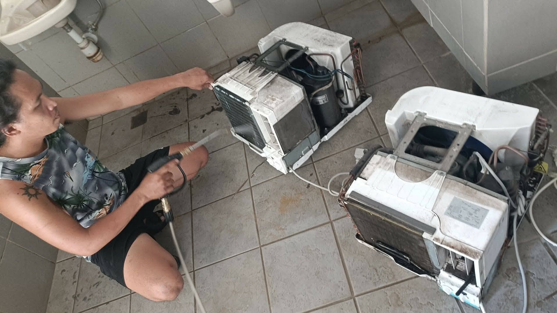 Technician pressure-washing two disassembled window-type air conditioners.