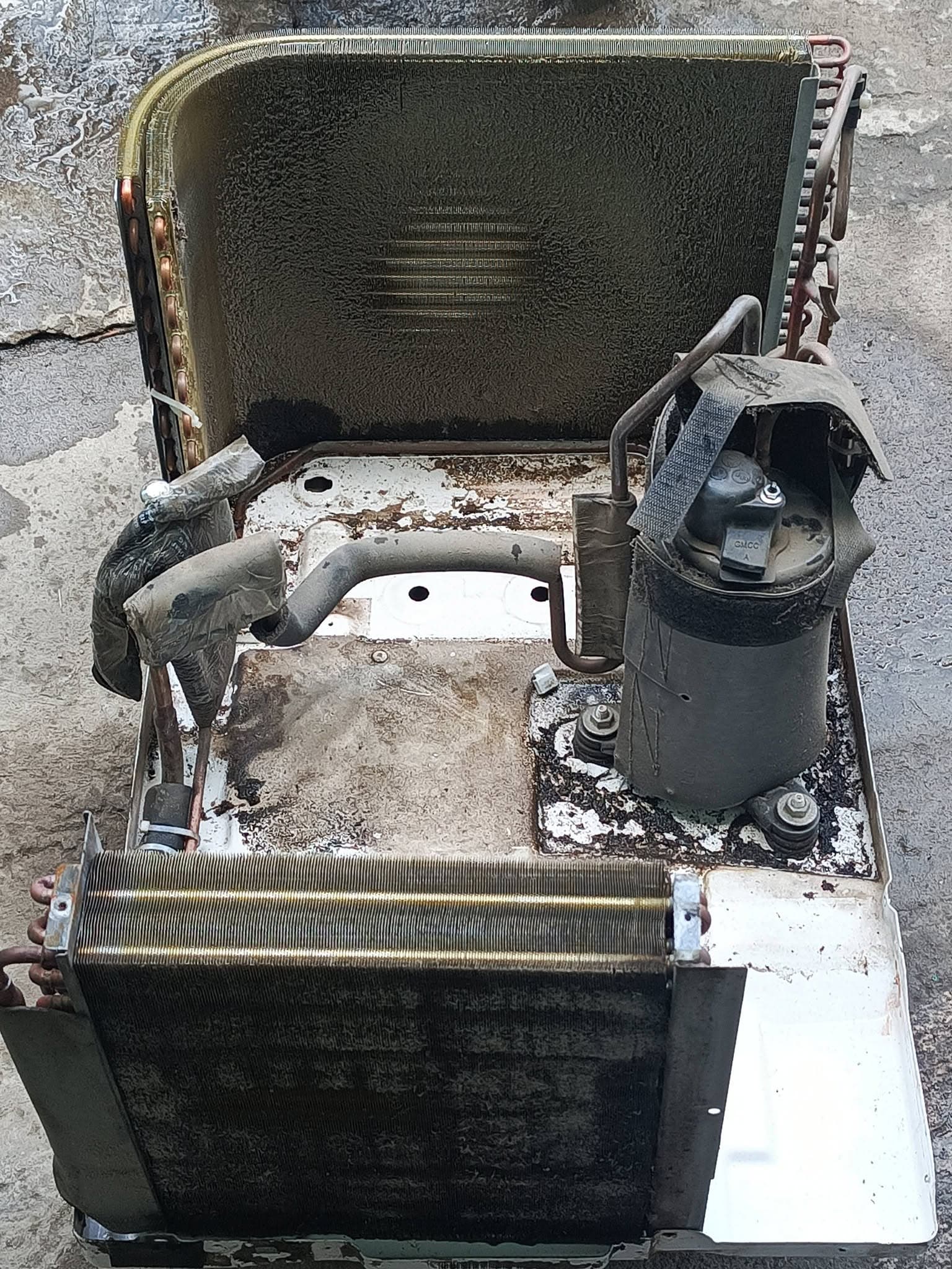 Opened window air conditioner exposing dirty coils, compressor, tubing, and corroded base pan.