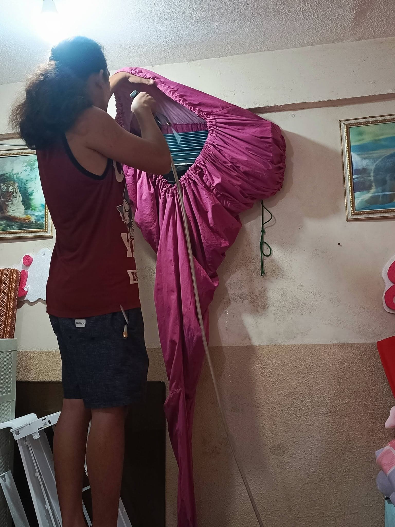 Technician fitting a protective wash cover around an indoor split-type air conditioner.