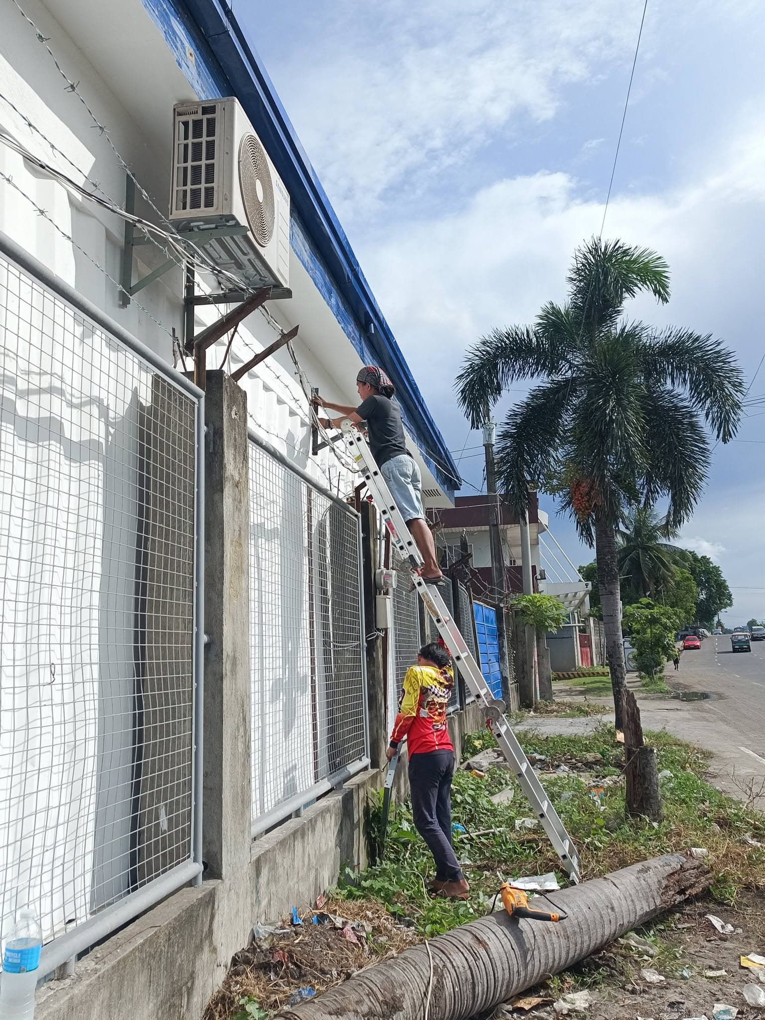 Technicians using an extension ladder to route refrigerant lines along a commercial building exterior.