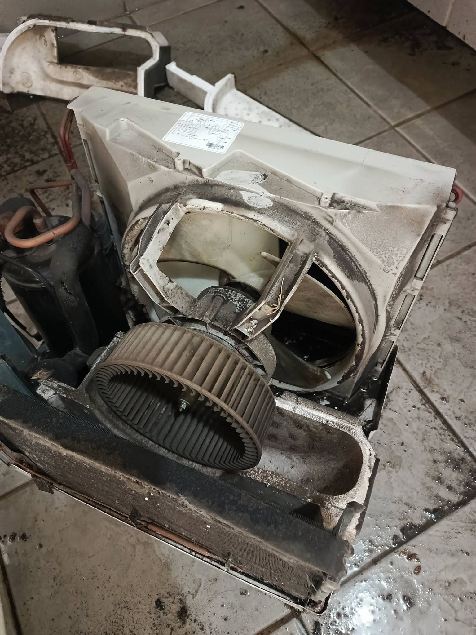 Disassembled window air conditioner exposing a dusty blower wheel and internal housing.