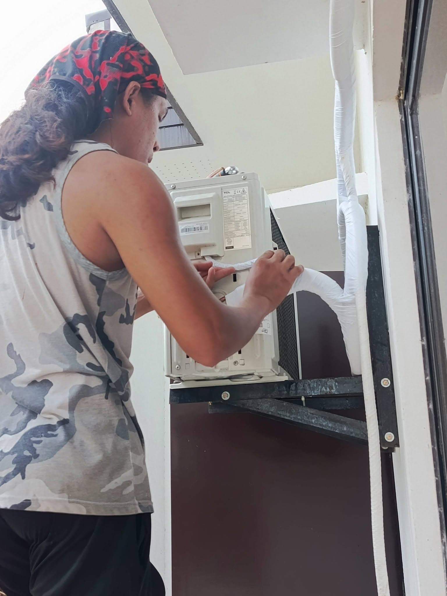 Technician wrapping and securing insulated lines beside the outdoor condenser.