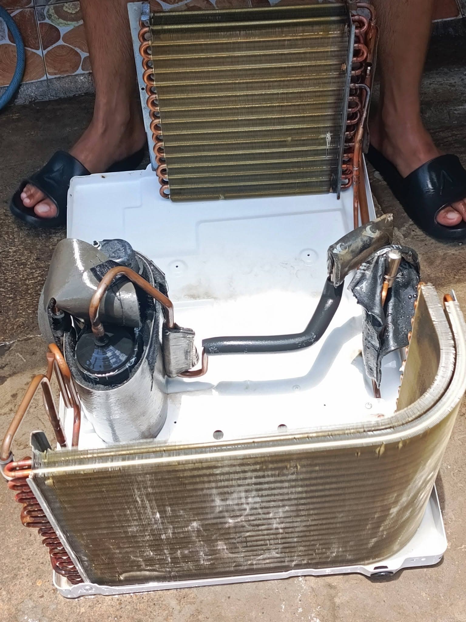 Fully stripped window air conditioner showing coils, compressor, tubing, and cleaned base pan.