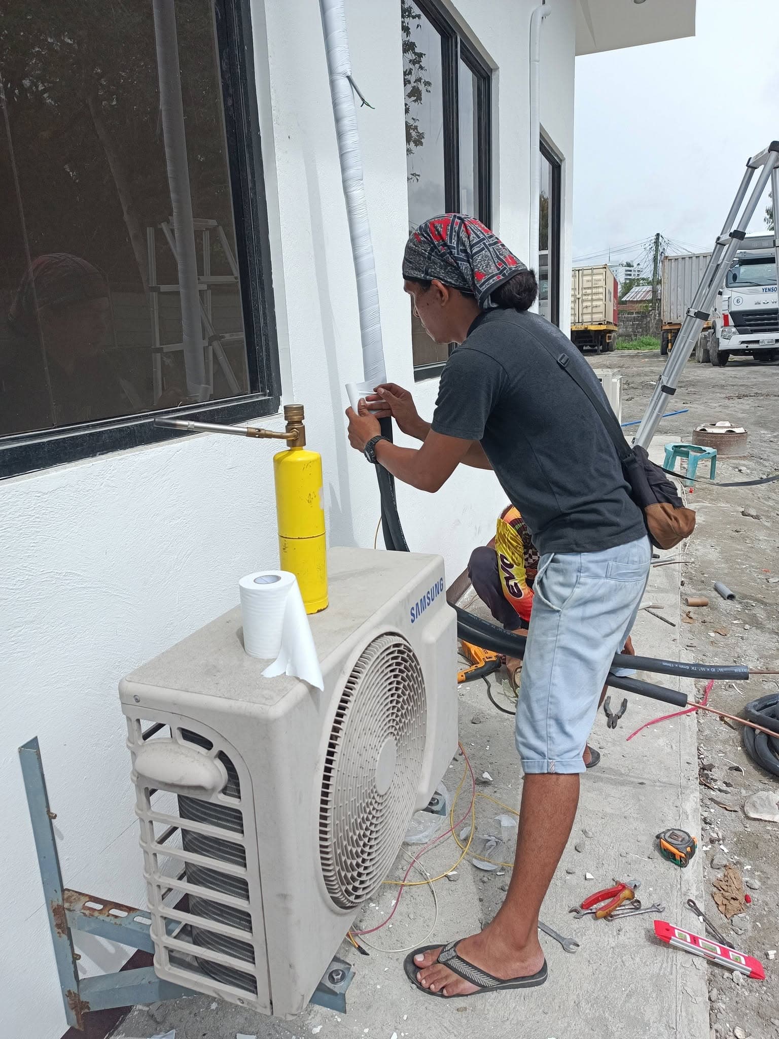 Technician finishing protective insulation on the refrigerant line set beside an outdoor condenser.