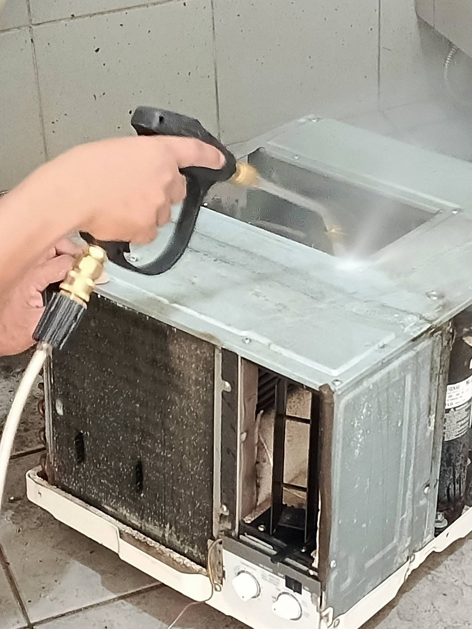 Close view of a technician pressure-washing the casing and coil of a window air conditioner.