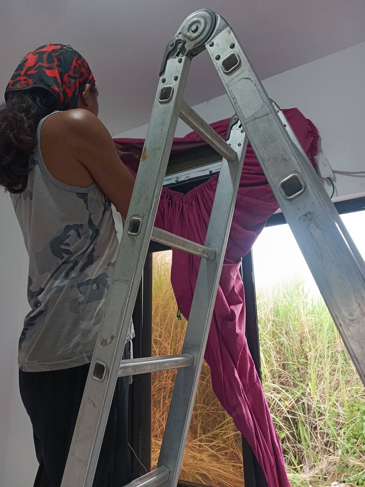 Technician finishing the indoor split-type air-conditioning unit above a window.