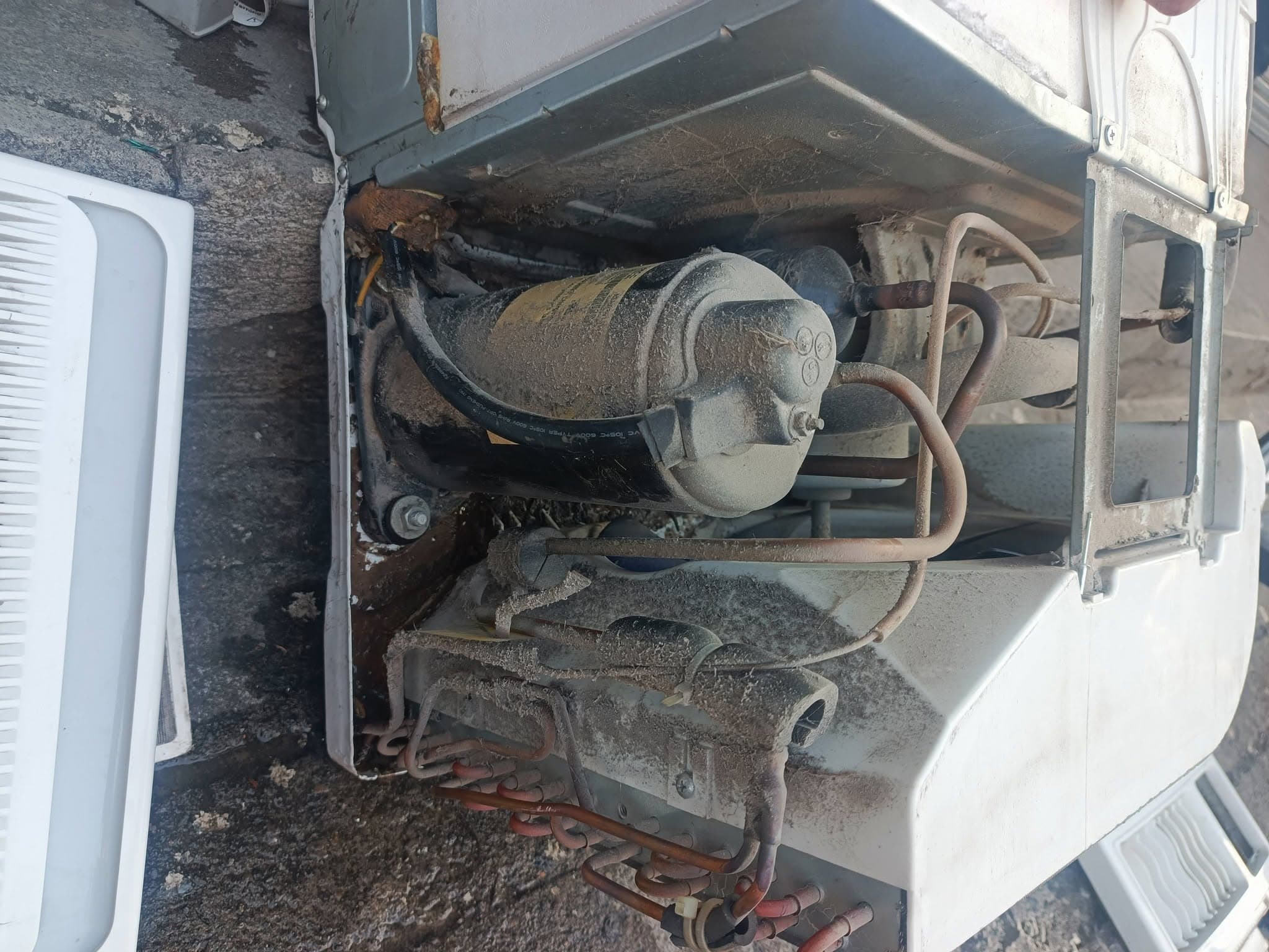 Dust-coated compressor, tubing, fan housing, and electrical components inside the window air conditioner.