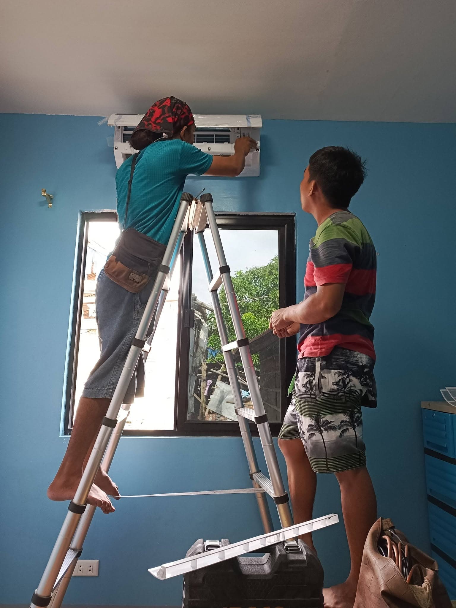 Technician installing and aligning the indoor split-type air-conditioning unit above a window.