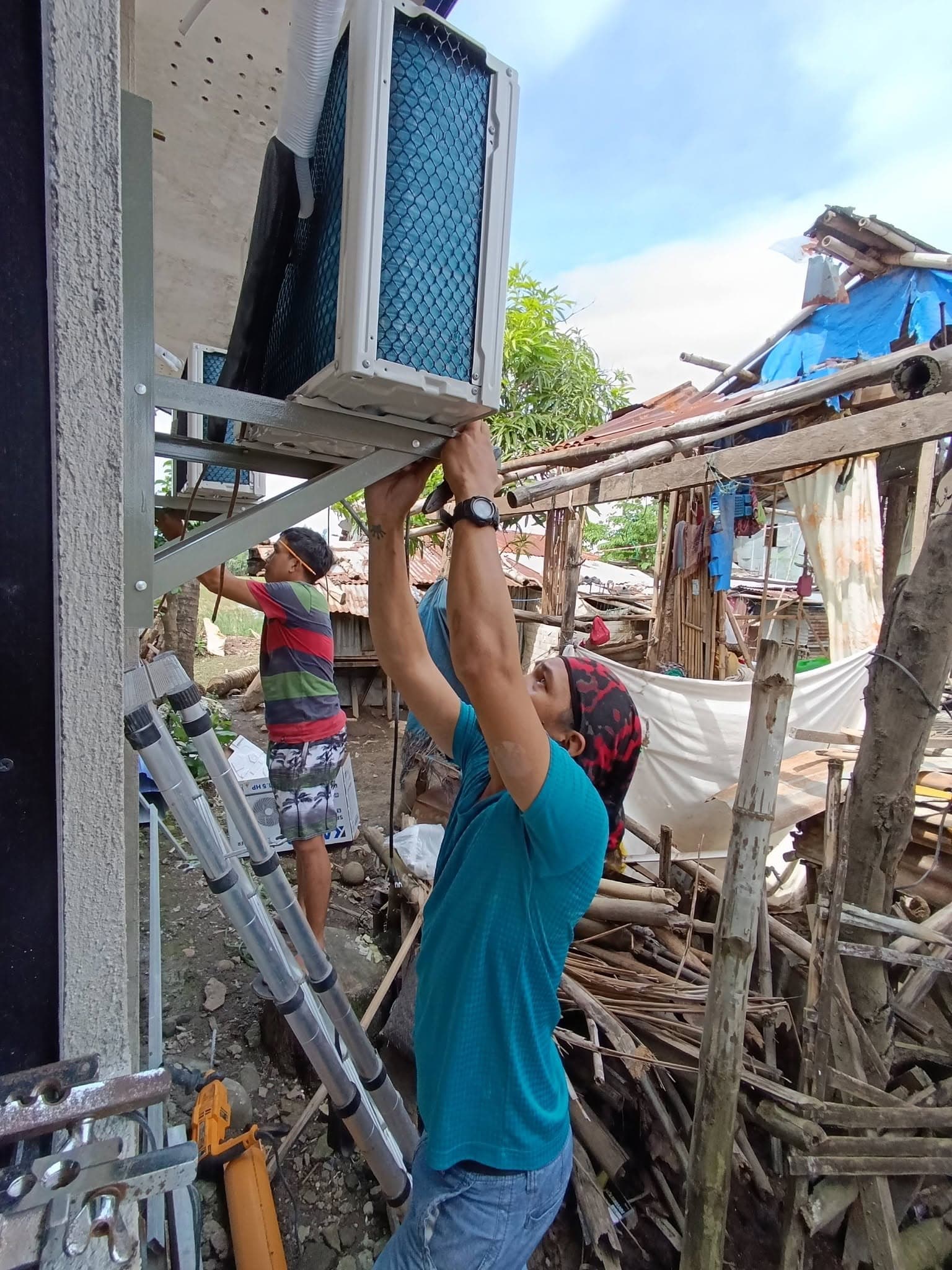 Technicians securing outdoor condenser units to galvanized steel wall brackets.