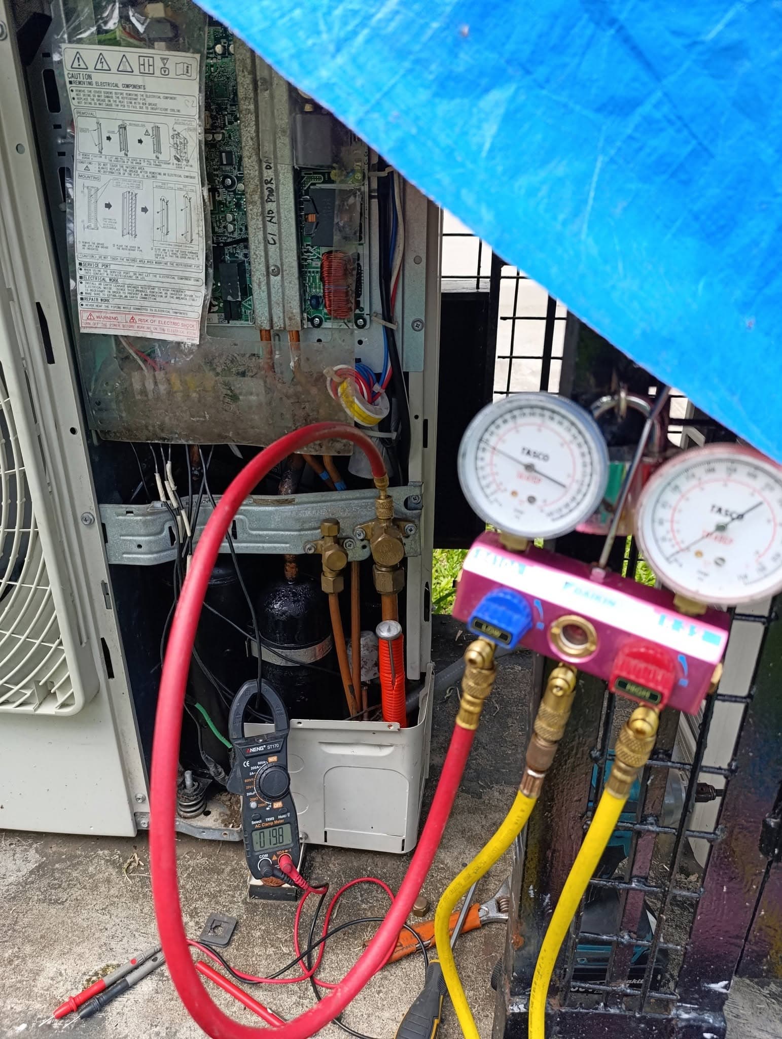 Air-conditioning system connected to manifold gauges and a clamp meter for diagnostics.