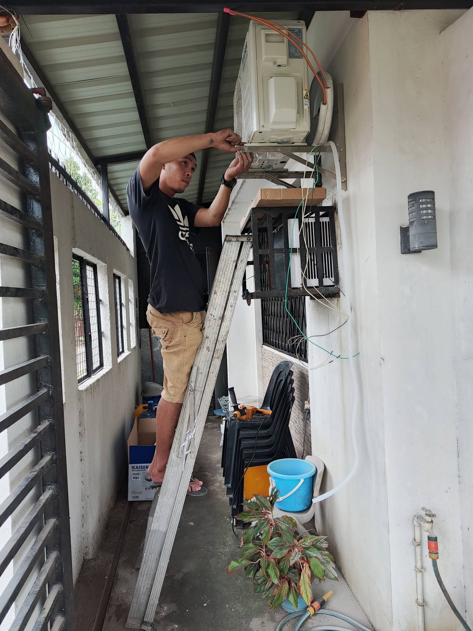 CALA owner Chuckie Amihan completing electrical and refrigerant connections on a wall-mounted outdoor air-conditioning unit.